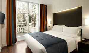 Et moderne hotellrom med en stor seng, mørke gardiner og et vindu ut mot en balkong. (AI-generert tekst)