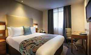 Hotellrom med en stor seng, skrivebord og stol. (AI-generert tekst)