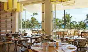 En restaurant med uteservering og utsikt over palmer og havet. (AI-generert tekst)