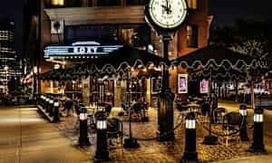 En uteservering ved en restaurant eller hotell med skilt og klokke, kveldsbelysning. (AI-generert tekst)