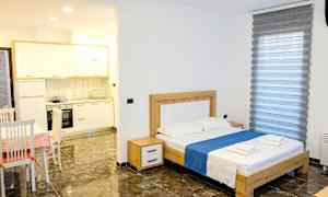 Et soverom med en dobbeltseng, bord med stoler og en liten kjøkkenkrok. (AI-generert tekst)