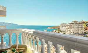 Utsikt fra en balkong mot havet, omgitt av boligblokker og en strand. (AI-generert tekst)