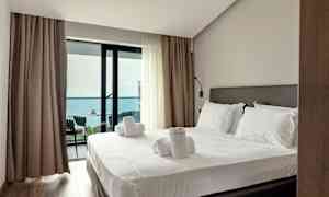 Et hotellrom med en oppredd seng og utgang til en balkong med havutsikt. (AI-generert tekst)