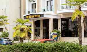 Bygningens front med teksten 'Hotel New Heaven', omgitt av palmer og en minibank. (AI-generert tekst)