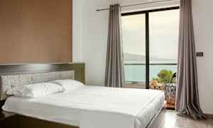 Et hotellrom med en seng, et vindu med gardiner og utsikt over havet. (AI-generert tekst)