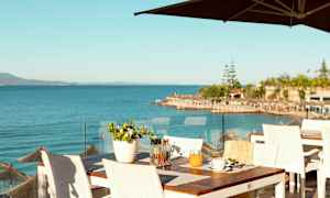 Utsikt over havet fra en restaurantterrasse med hvite bord og stoler. (AI-generert tekst)