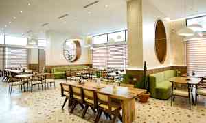 En lys restaurant med grønne sitteplasser og trebord. (AI-generert tekst)