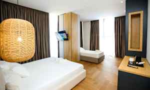 Et hotellrom med to senger, en hengende lampe, en veggmontert TV og et skrivebord med en kaffetrakter. (AI-generert tekst)