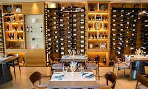 Vinflasker arrangert i hyller bak spisebord. (AI-generert tekst)