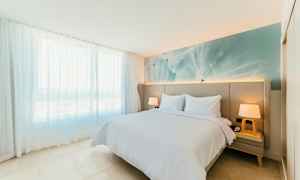 Lyst og moderne innredet soverom med en dobbeltseng, to nattbord og en stor vinduspanel med delikate hvite gardiner. (AI-generert tekst)