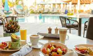 Frokost med grønnsakswrap, fruktsalat og drikker ved et uteområde med basseng. (AI-generert tekst)