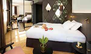 Et hotellrom med en stor seng, veggdekorasjoner og et speil som reflekterer rommet. En koffert står ved siden av, og det finnes en liten kaktus på et bord. (AI-generert tekst)