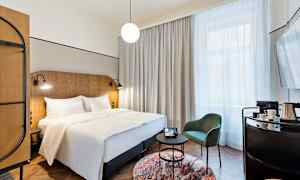 Et hotellrom med en dobbeltseng, en stol og et bord samt et stort vindu med gardiner. (AI-generert tekst)