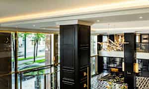 En elegant hotellobby med moderne detaljer, mørke søyler, og store vinduer med utsikt mot gaten utenfor. (AI-generert tekst)