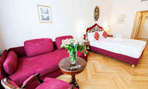 Et hotellrom med en rød sofa, et rundt bord med en blomsterbukett og en seng med røde detaljer. (AI-generert tekst)