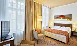 Et hotellrom med en dobbeltseng, en lenestol, et bord med TV på og store vinduer med gardiner. (AI-generert tekst)