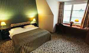 Et hotellrom med en dobbeltseng, stripete sengeteppe, to nattbord med lamper og en arbeidsbenk med stol ved et vindu. (AI-generert tekst)