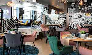 En moderne interiør av en restaurant med fargerike stoler rundt bord som har dekketallerkener og glass. Veggene er dekorert med kunstneriske mønstre og tekster. (AI-generert tekst)