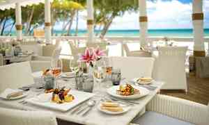 Et dekket restaurantbord nær stranden med tallerkener, glass og blomster. (AI-generert tekst)