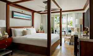 Et elegant soverom med en himmelseng, sittemøbler og utsikt over frodige planter gjennom åpne glassdører. (AI-generert tekst)