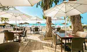 Utendørs servering med tremøbler og parasoller, plassert nær stranden med utsikt over havet. (AI-generert tekst)