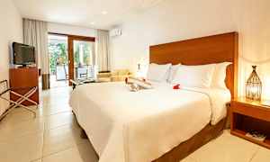 Et hotellrom med stor seng, TV, sitteområde og en terrasse med utsikt mot en hage. (AI-generert tekst)