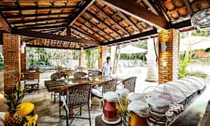 En åpen restaurant med tre- og teglstruktur, hvor mat og fat er lagt ut på et bord sammen med fruktdrikker. En person står ved et bord. (AI-generert tekst)