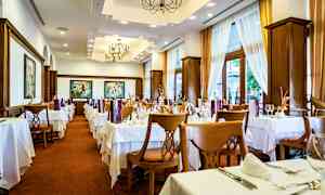 Interiør av en restaurant med dekkede bord og stoler, lyse gardiner og dekorative taklamper. (AI-generert tekst)