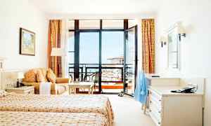 Et hotellrom med to enkeltsenger, en sofa, et skrivebord og en balkong med utsikt. (AI-generert tekst)