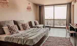 Et lyst og moderne hotellrom med seng, sofa og en balkong med utemøbler. (AI-generert tekst)