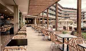 En utendørs restaurant med rottingmøbler og utsikt over et basseng og solsenger. (AI-generert tekst)