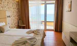 Et hotellrom med en dobbeltseng oppredd med hvite laken og dekorert med håndklær. Det er et vindu med utsikt mot havet. (AI-generert tekst)