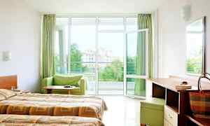 Hotellrom med dobbeltsenger, skrivebord og åpent vindu mot en balkong med utsikt. (AI-generert tekst)