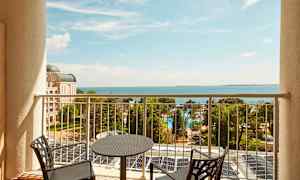 Utsikt fra en balkong mot havet, med stoler og bord i forgrunnen. (AI-generert tekst)