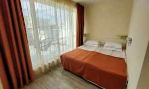 Et hotellrom med to enkeltsenger, dekket med et oransje teppe, og store vinduer som vender mot en balkong. (AI-generert tekst)