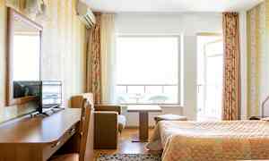 Et hotellrom med to senger, et skrivebord i tre med en TV på, en liten sofahjørne med salongbord og en balkong i bakgrunnen. (AI-generert tekst)