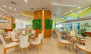 En restaurantinteriør med flere bord og stoler, dekorative veggpaneler med grønt og store glassvegger. (AI-generert tekst)