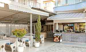 Utendørs serveringsområde med bord og stoler, omgitt av planter og en bardisk. (AI-generert tekst)