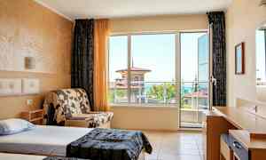 Et hotellrom med to enkeltsenger, en sofa og et skrivebord, med store vinduer som viser utsikt mot havet. (AI-generert tekst)