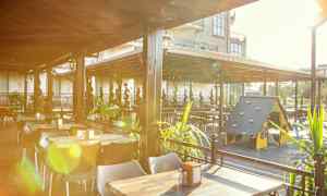 En utendørsrestaurant med bord, stoler og en lekeplass for barn under et tak. (AI-generert tekst)