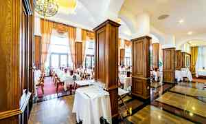 En elegant restaurant med dekkede bord, mørke tregulv og store vinduer med gardiner. (AI-generert tekst)