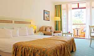 Et hotellrom med en dobbeltseng, sittegruppe med lenestol og bord, samt en balkong med møbler og utsikt. (AI-generert tekst)