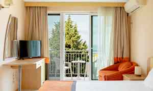 Et hotellrom med balkong, seng, lenestol og TV. (AI-generert tekst)