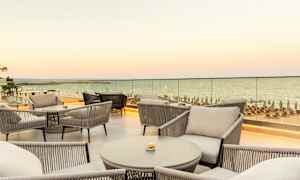 Utsikt over møblert terrasse med sitteplasser og sjø i bakgrunnen. (AI-generert tekst)