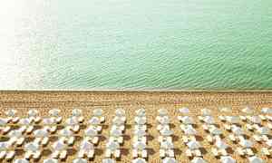 Strand med solsenger og parasoller ordnet i rader nær turkis hav. (AI-generert tekst)