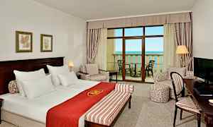 Et hotellrom med dobbeltseng, sittegruppe, et skrivebord og balkong med havutsikt. (AI-generert tekst)