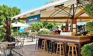 En kafé med bord og stoler utendørs ved Sunshine Café, med grøntområder og havutsikt i bakgrunnen. (AI-generert tekst)