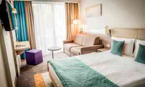 Et moderne hotellrom med en dobbeltseng, sofa og vindu med gardiner. (AI-generert tekst)