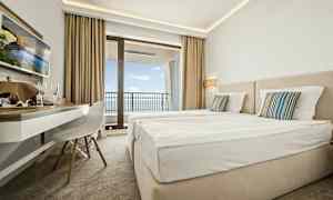 Hotellrom med to senger, skrivebord og balkong med utsikt over havet. (AI-generert tekst)