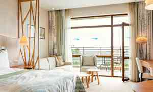 Et hotellrom med seng, sittegruppe, bord og åpen balkongdør. (AI-generert tekst)